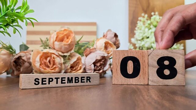 Hand placing wooden calendar blocks showing september 8 on a wooden table
