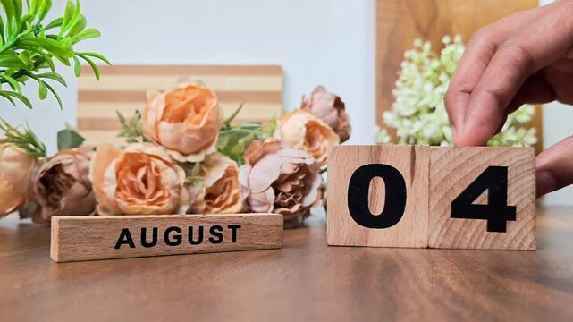 Hand placing wooden calendar blocks showing august 4 on a wooden table