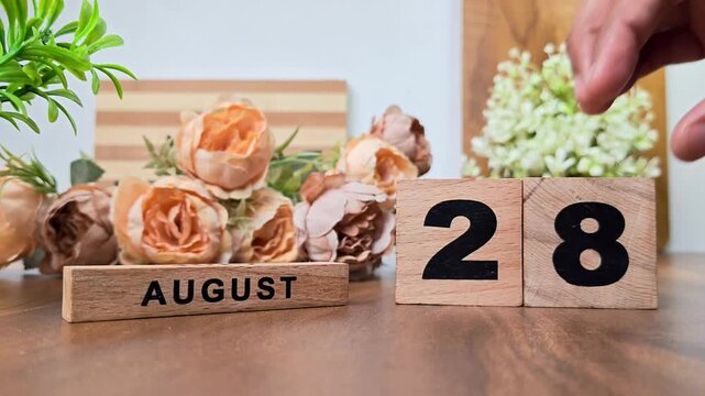 Hand placing wooden calendar blocks showing august 28 on a wooden table