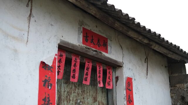 Weathered rural house with red Spring Festival couplets and blessings on doorway in Guangxi China. Traditional Chinese New Year decoration. Concept of festive culture, rural heritage, folk tradition