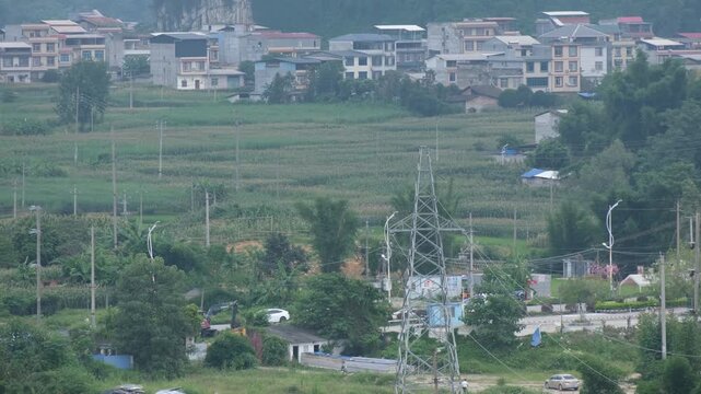 Rural village with farmland, power transmission tower and scattered houses on a hillside in Yizhou Guangxi China. Chinese countryside landscape. Agricultural heritage, regional infrastructure concept