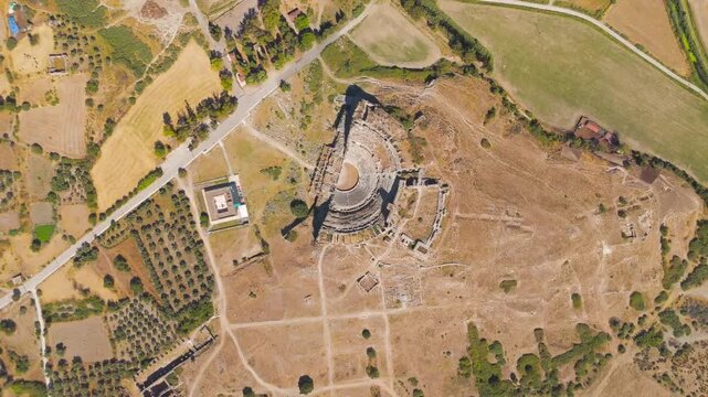 Balat, Turkey. The ancient theatre of Miletus, a vast semicircular stone amphitheatre rising from the arid landscape, captured in a steady top-down aerial view under bright summer sun. Aerial View, H