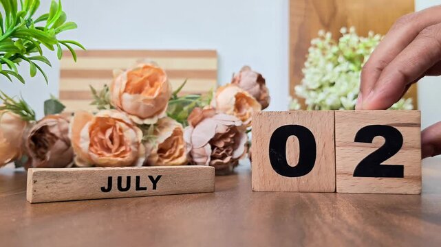 Hand placing wooden calendar blocks showing july 2 on a wooden table