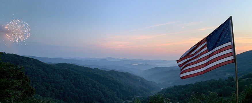 American flag waves over misty mountains at sunrise with fireworks