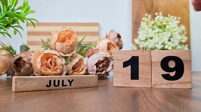 Hand placing wooden calendar blocks showing july 19 on a wooden table