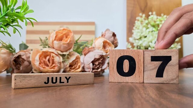 Hand placing wooden calendar blocks showing july 7 on a wooden table