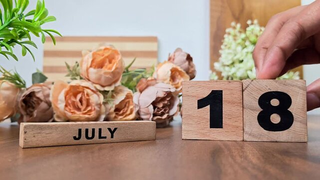 Hand placing wooden calendar blocks showing july 18 on a wooden table
