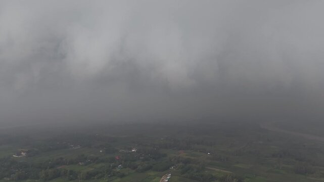 Aerial view of a rural landscape shrouded in thick fog and low clouds over green fields and