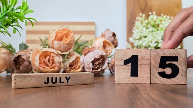 Hand placing wooden calendar blocks showing july 15 on a wooden table