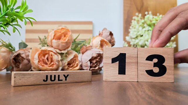 Hand placing wooden calendar blocks showing july 13 on a wooden table