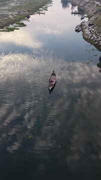 Serene aerial view of a lone wooden boat navigating a calm river reflecting the cloudy sky and