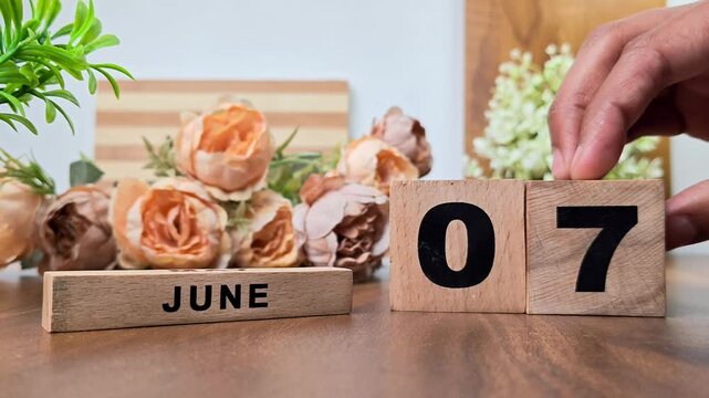 Hand placing wooden calendar blocks showing june 7 on a wooden table
