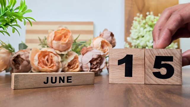 Hand placing wooden calendar blocks showing june 15 on a wooden table