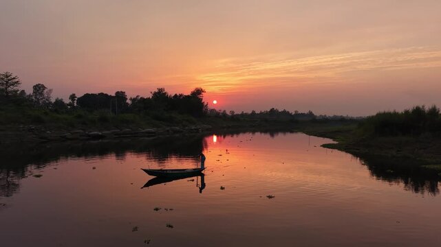 Serene sunset over tranquil river with lone fisherman in traditional boat casting net peaceful