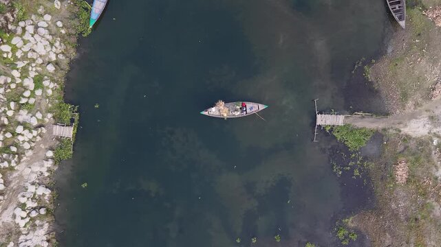 Aerial drone view of traditional fishing boat on calm river with wooden pier and rocky shore