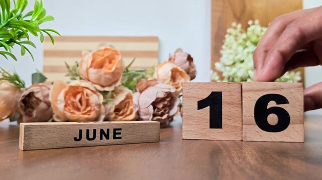Hand placing wooden calendar blocks showing june 16 on a wooden table