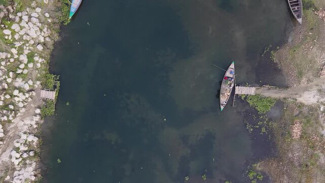 Aerial drone view of traditional wooden fishing boat docked at rustic pier on calm river water