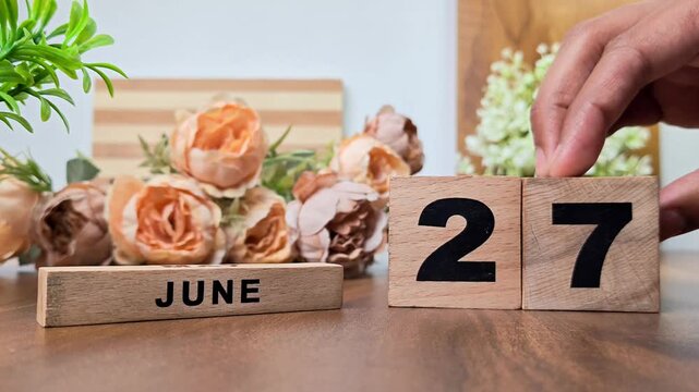 Hand placing wooden calendar blocks showing june 27 on a wooden table