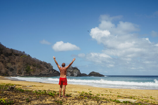 Man with arms raised on the beach, Fernando de Noronha, Pernambuco, Brazil