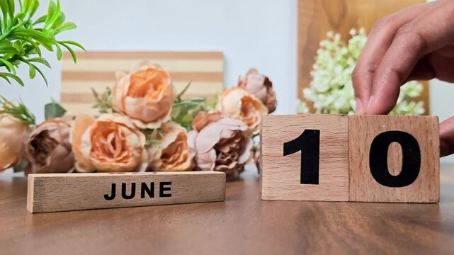 Hand placing wooden calendar blocks showing june 10 on a wooden table