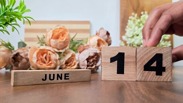 Hand placing wooden calendar blocks showing june 14 on a wooden table