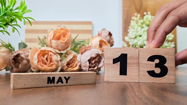 Hand placing wooden calendar blocks showing may 13 on a wooden table