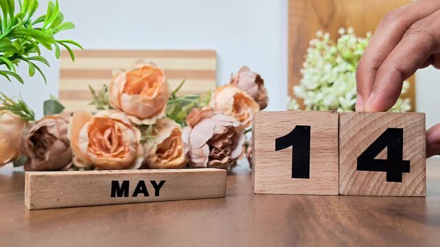 Hand placing wooden calendar blocks showing may 14 on a wooden table