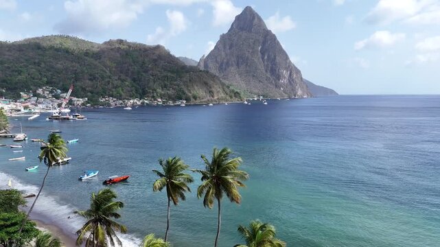Stunning drone along a tropical beach with green palm trees looking towards the grand volcanic Pitons in Saint Lucia