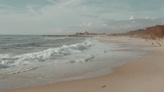 Waves Rolling Onto the Sandy Beach at Sao Pedro de Maceda in Ovar Portugal with a Village on the Horizon