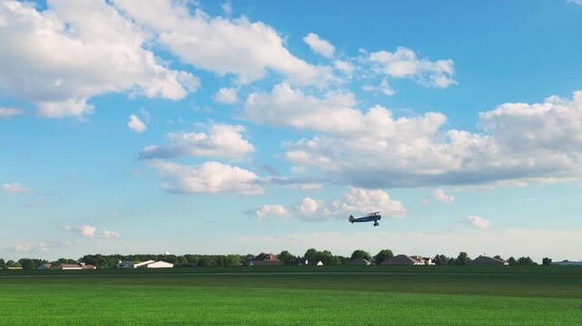 A blue biplane taking off and flying over a grass field up into a sunny sky.