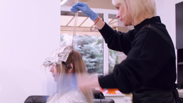 Hairdresser highlighting. Hair routine. Professional master working with female client using blow dryer providing treatment at workplace.