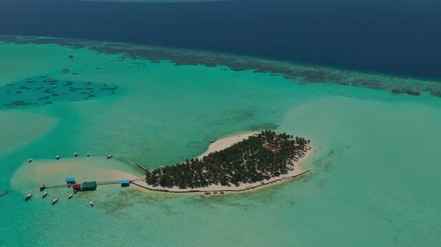 Aerial drone flight flying backwards away from Onuk Island, Balabac, Palawan, Philippines. Pull away tracking shot reveals remote tropical paradise, stilt houses, and coral reef topography.
