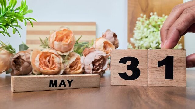 Hand placing wooden calendar blocks showing may 31 on a wooden table