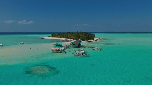 Aerial slow approach toward the wooden dock of Onuk Island, Balabac, Palawan, Philippines. Drone pushes forward over crystal clear shallow turquoise sea revealing tropical island resort.