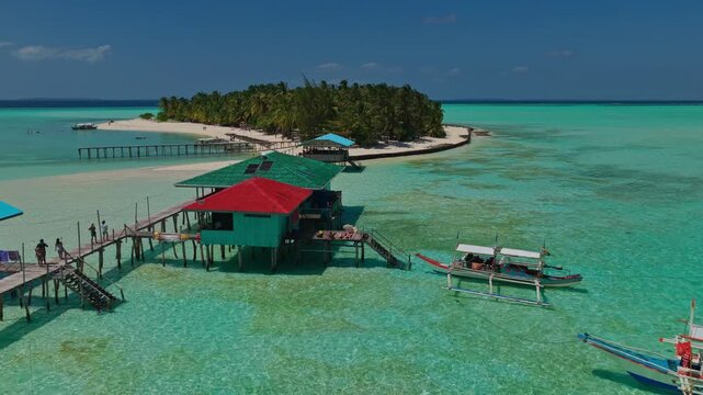 Aerial view flying around the wooden dock of Onuk Island in Balabac, Palawan, Philippines. Drone tracks over rustic jetty, crystal clear turquoise water, and tropical reef at remote beach resort.