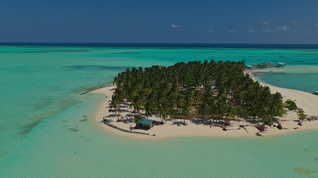 Aerial forward ascend over Onuk Island stilt houses at sunrise, Balabac, Palawan, Philippines. Drone rises over tropical white sandbar, overwater bungalows, and clear turquoise sea at morning.