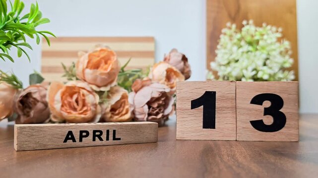 Hand placing wooden calendar blocks showing april 13 on a wooden table