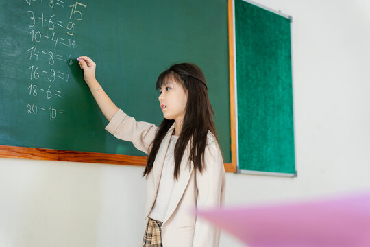 Young student writing math equations on blackboard in classroom, Smart schoolgirl solving math problems on chalkboard in school, Education concept with girl learning mathematics in the classroom