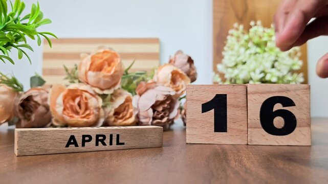 Hand placing wooden calendar blocks showing april 16 on a wooden table