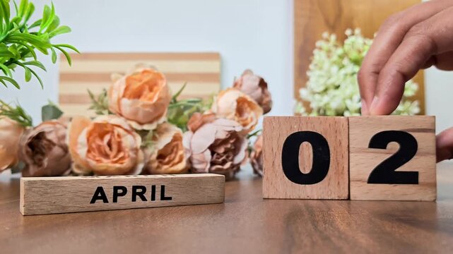 Hand placing wooden calendar blocks showing april 2 on a wooden table