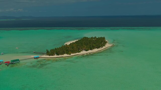 Long distance aerial drone orbit shot moving clockwise around Onuk Island in Balabac Palawan Philippines during early morning sunrise with warm golden hour light reflecting on calm ocean water