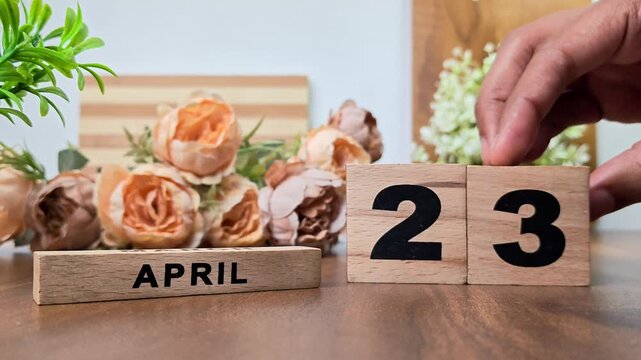 Hand placing wooden calendar blocks showing april 23 on a wooden table