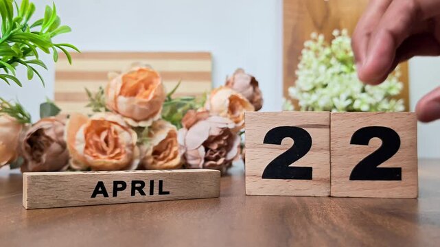 Hand placing wooden calendar blocks showing april 22 on a wooden table
