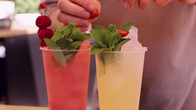 Fruit drinks. Refreshing beverages. Unrecognizable barman hands using mint leaves raspberries with crushed ice at professional bar counter.
