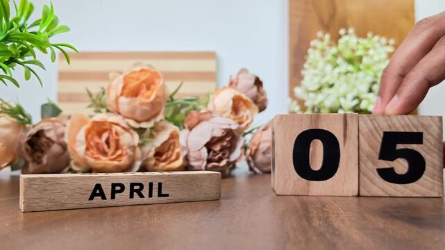 Hand placing wooden calendar blocks showing april 5 on a wooden table