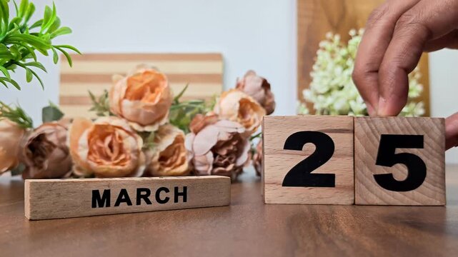 Hand placing wooden calendar blocks showing march 25 on a wooden table