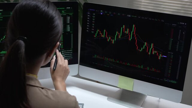 Focused woman trader analyzing financial stock market chart data on computer monitor screen inside dark office