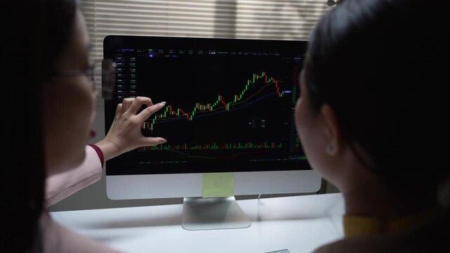 Serious analyst and trader discussing stock chart on computer screen during dark office finance meeting