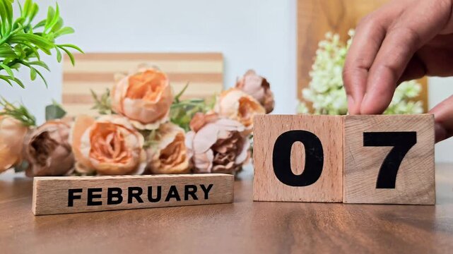 Hand placing wooden calendar blocks showing february 7 on a wooden table