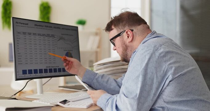 Man analyst overweight focused on finance analysis. He points at charts on computer, checks paperwork, updates budget forecasts in a tidy office. Concept highlights precise financial review.